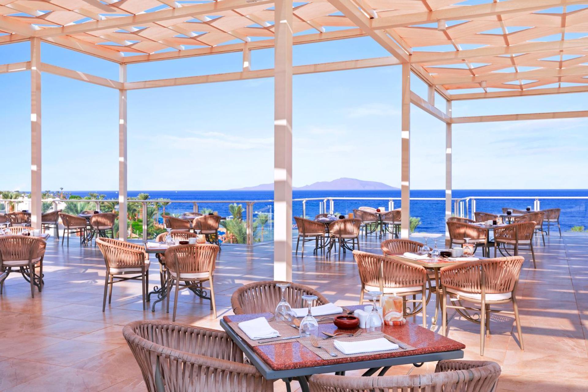 Pickalbatros Royal Grand Sharm - Adults Friendly 16 Years Plus Exterior photo The photo shows a spacious outdoor restaurant with a beautiful view of the ocean. The seating area features several tables and wicker chairs. The open design includes a wooden pergola providing some shade, while large windows or openings allow for a 