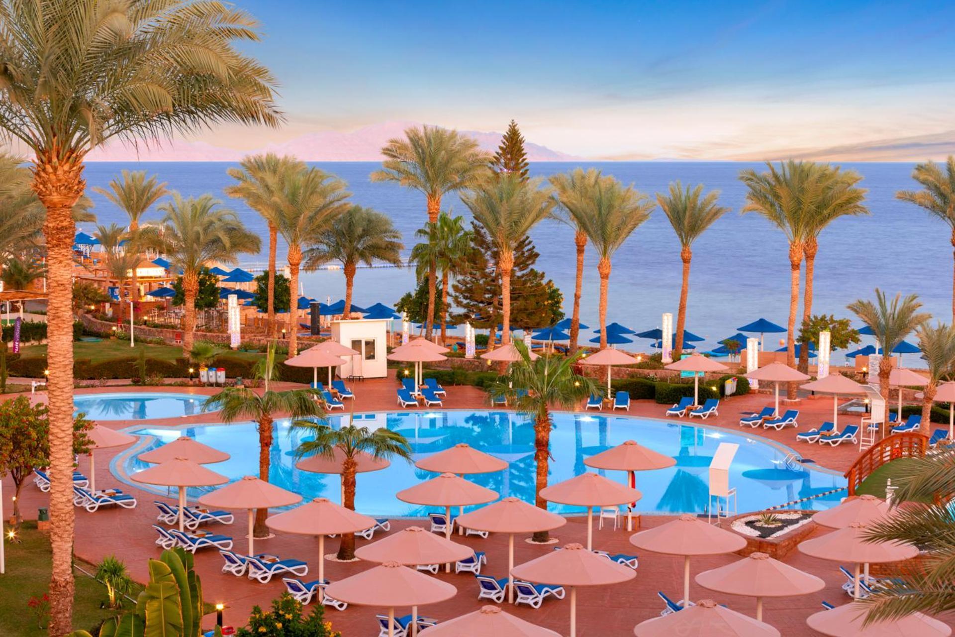 Pickalbatros Royal Grand Sharm - Adults Friendly 16 Years Plus Exterior photo The photo shows a beautiful resort scene with a swimming pool surrounded by lounge chairs and umbrellas. Palm trees line the area, adding to the tropical atmosphere. In the background, there is a view of the sea under a clear sky, suggesting a peacef