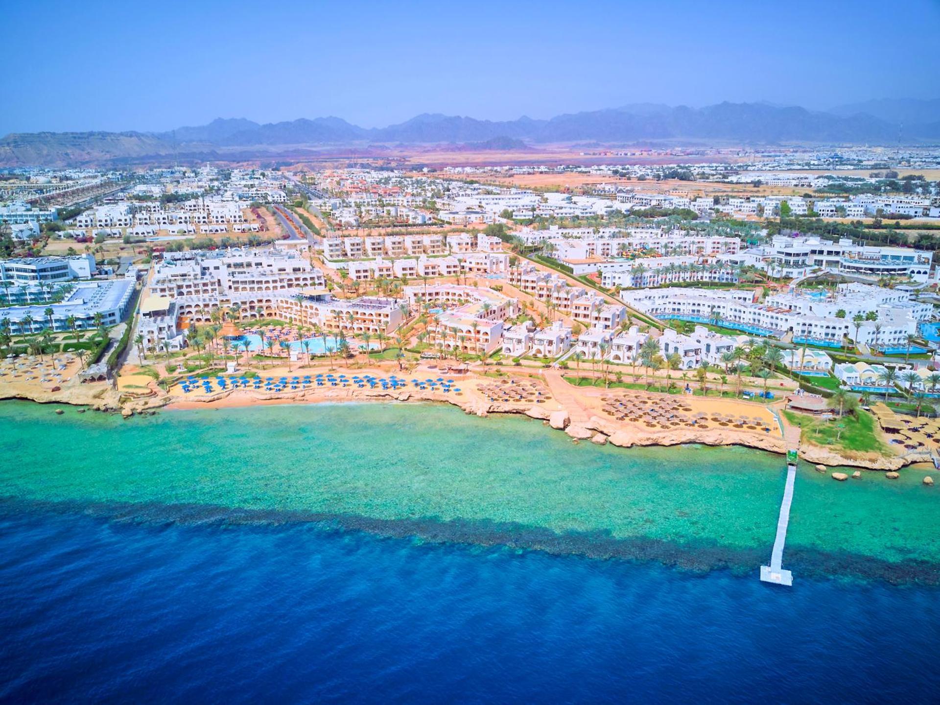 Pickalbatros Royal Grand Sharm - Adults Friendly 16 Years Plus Exterior photo The photo shows an aerial view of a coastal resort area. In the foreground, there is a clear blue ocean with a gradient of colors from deep blue to lighter shades near the shore. The beach features sandy areas lined with sun loungers and umbrellas. F