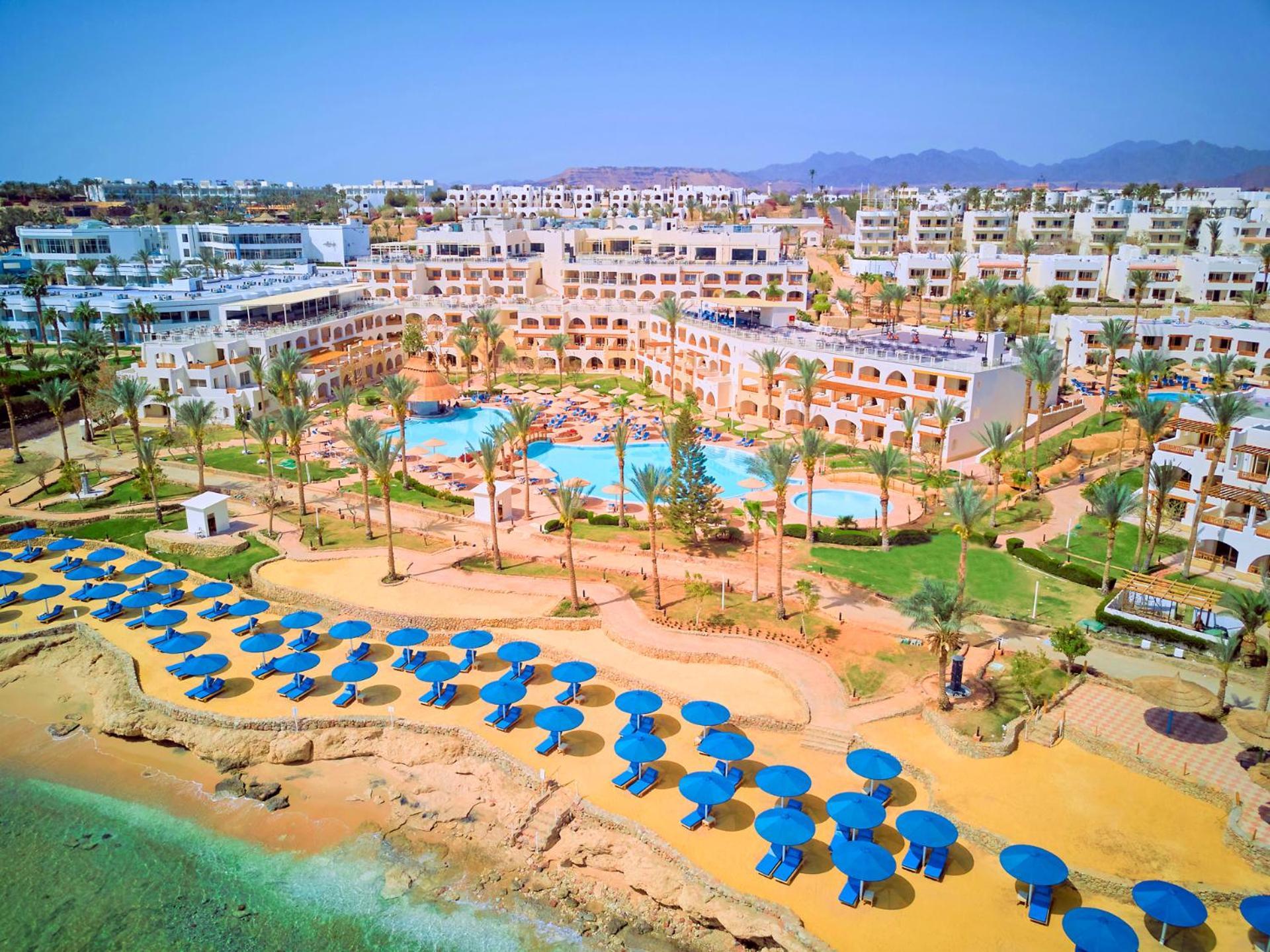 Pickalbatros Royal Grand Sharm - Adults Friendly 16 Years Plus Exterior photo The photo shows a vibrant resort area with several buildings that appear to be accommodations or hotel units. There are multiple swimming pools surrounded by palm trees, creating a tropical atmosphere. In the foreground, there is a beach area with sa