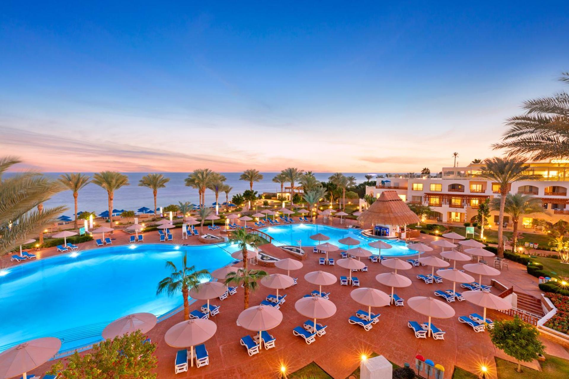 Pickalbatros Royal Grand Sharm - Adults Friendly 16 Years Plus Exterior photo The photo showcases a luxurious resort setting with two large swimming pools, surrounded by lounge chairs and umbrellas. Palm trees are interspersed around the pool area, enhancing the tropical feel. In the background, there’s a view of the ocean, an
