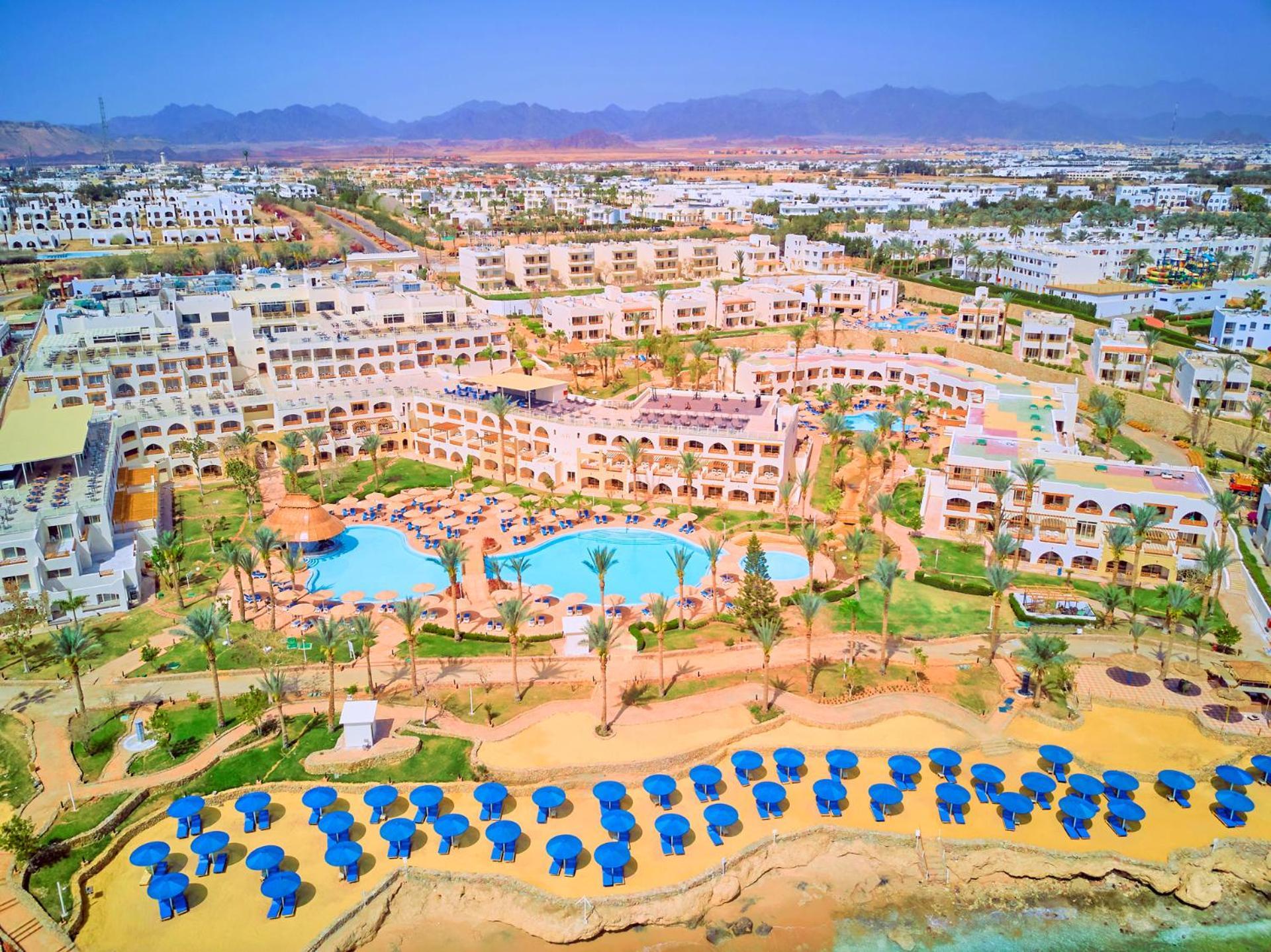 Pickalbatros Royal Grand Sharm - Adults Friendly 16 Years Plus Exterior photo The photo shows a large resort complex set in a scenic location, likely near a beach. The layout features multiple buildings with a Mediterranean style of architecture, surrounded by lush greenery and palm trees. Central to the resort is a swimming p
