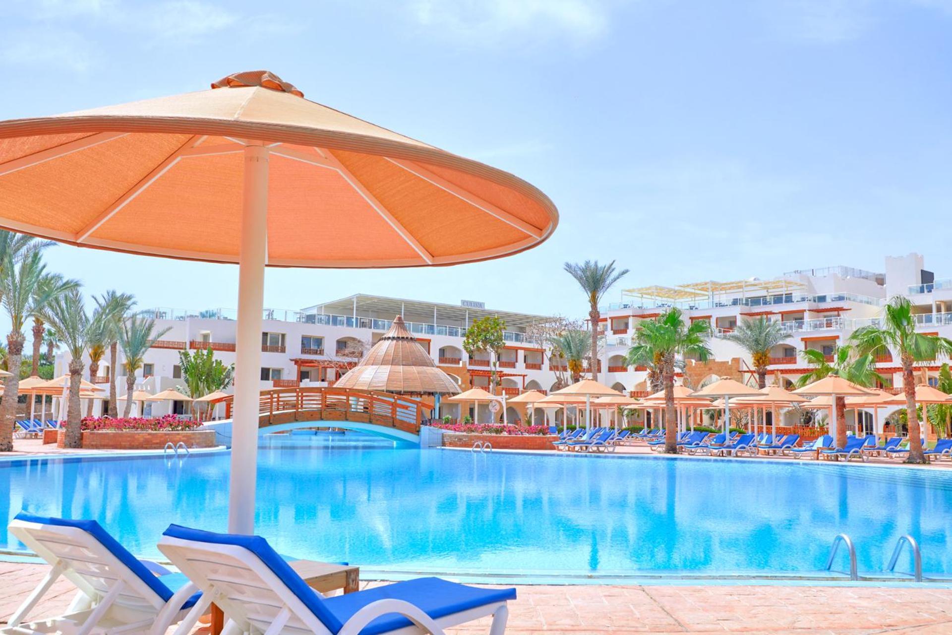Pickalbatros Royal Grand Sharm - Adults Friendly 16 Years Plus Exterior photo The photo shows a picturesque resort scene featuring a large swimming pool surrounded by lounge chairs and umbrellas. The pool is shimmering under a bright blue sky, and there are several palm trees in the background, adding to the tropical atmospher