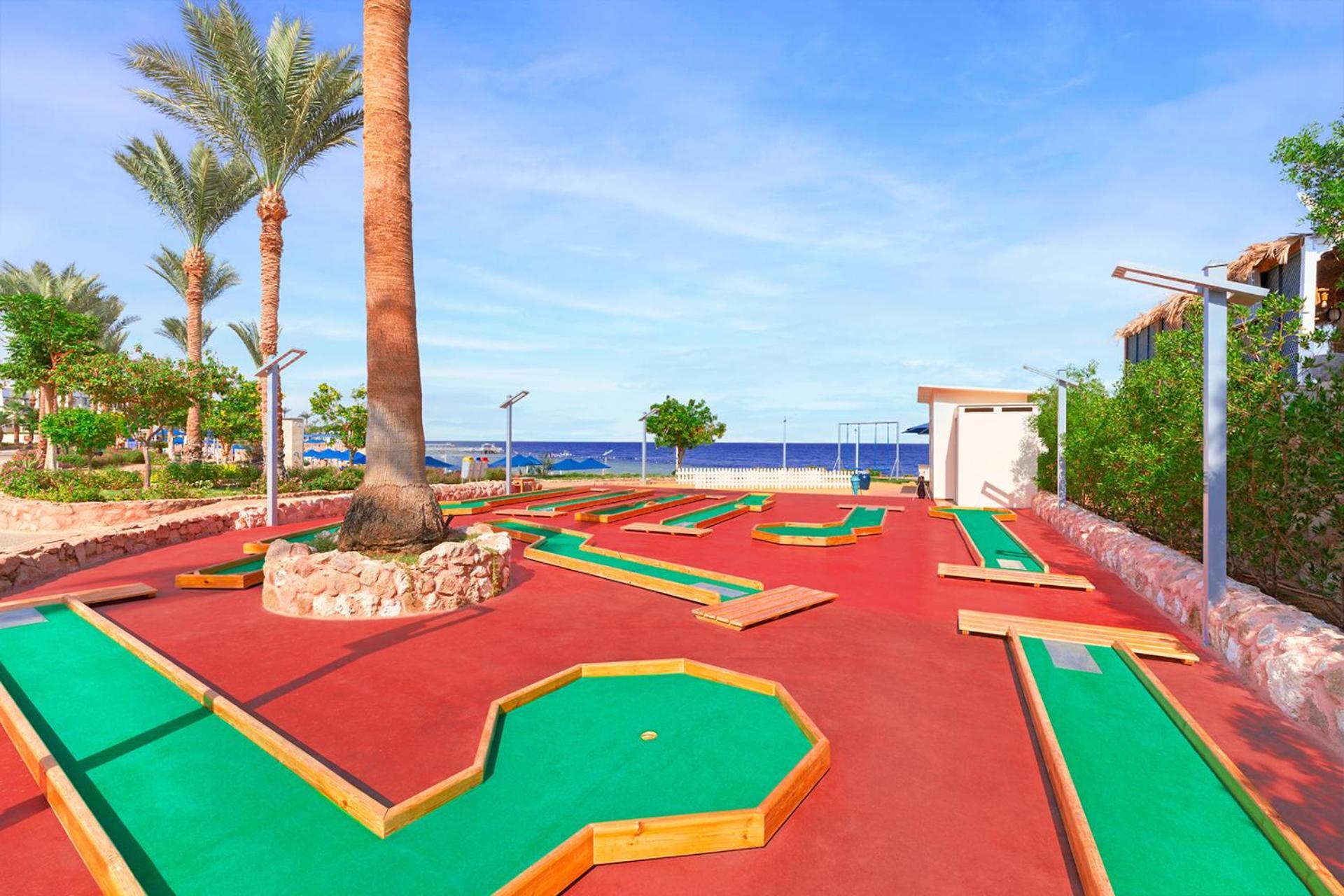 Pickalbatros Royal Grand Sharm - Adults Friendly 16 Years Plus Exterior photo The photo shows a mini-golf course situated outdoors, with a view of the sea in the background. The course features vibrant green and red surfaces, laid out in winding patterns, and surrounded by well-maintained landscaping, including palm trees. The