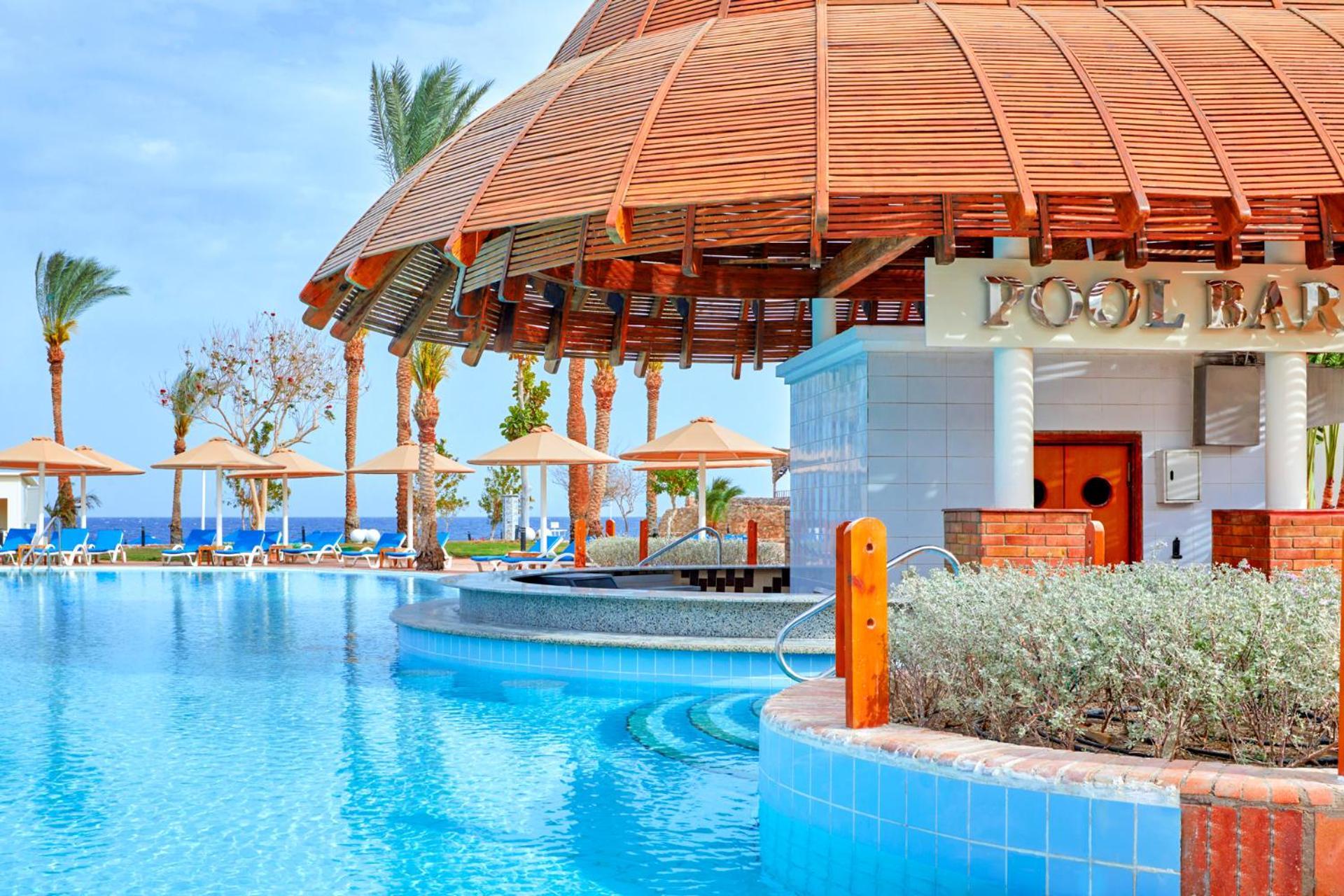 Pickalbatros Royal Grand Sharm - Adults Friendly 16 Years Plus Exterior photo The photo depicts a picturesque pool area at a resort. In the foreground, there is a clear and inviting swimming pool with curved edges, surrounded by a light blue tile border. To the side, a pool bar is visible with a wooden roof and stylish archite
